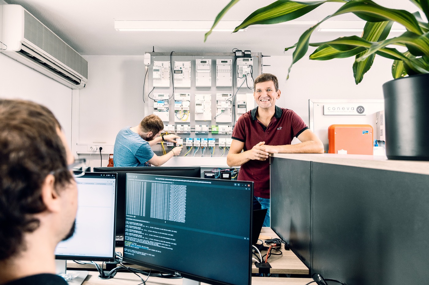 Developers at their desks in the EnQS Testlab, working next to a wall of metering equipment